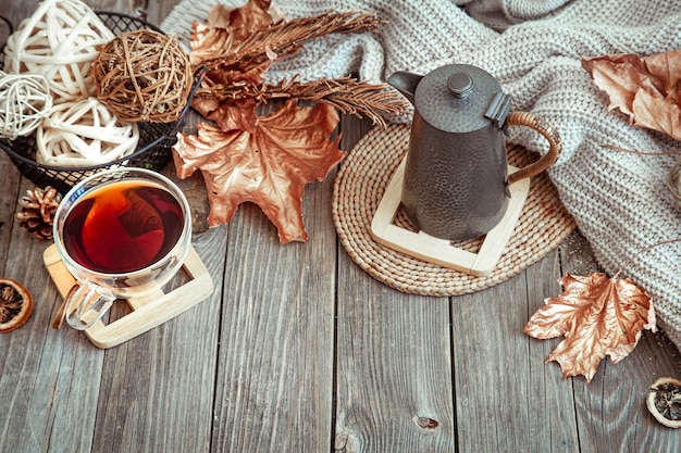 Glass cup with tea and teapot on wooden table with autumn decor details.