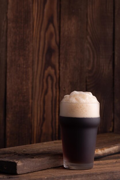 Glass of dark beer over a dark textured wooden background