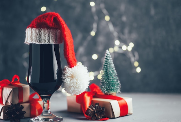 Стакан темного крафтового пива крепкий, носильщик в новогодней шапке на праздничном столе copyspace