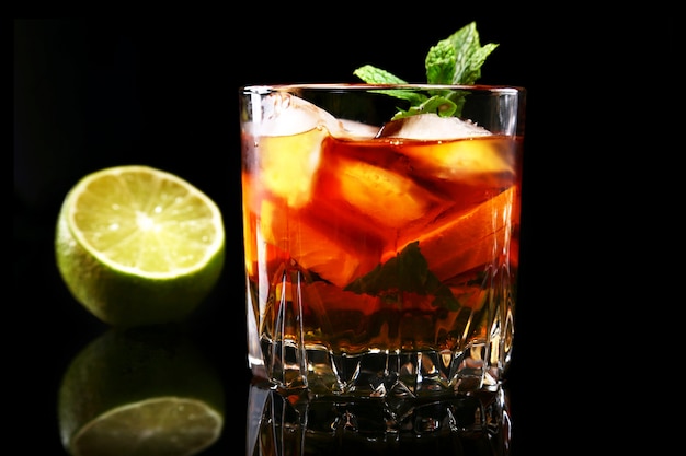 Glass of Dark Rum Cocktail with lime, orange, ice cubes and mint leaves .