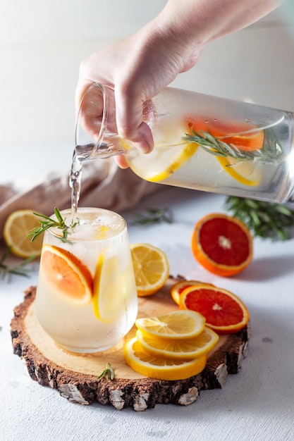 A glass and a decanter of lemonade Lemon and grapefruit slices with rosemary leaves in a drink