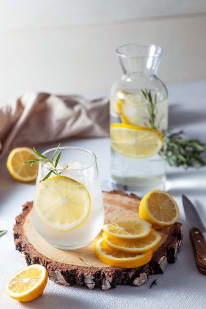 Un bicchiere e una caraffa di limonata fette di limone con foglie di rosmarino in una bevanda