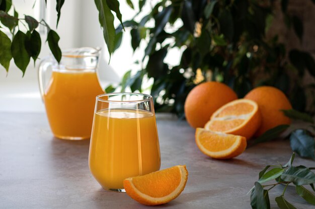 A glass and a decanter of orange juice next to fresh oranges