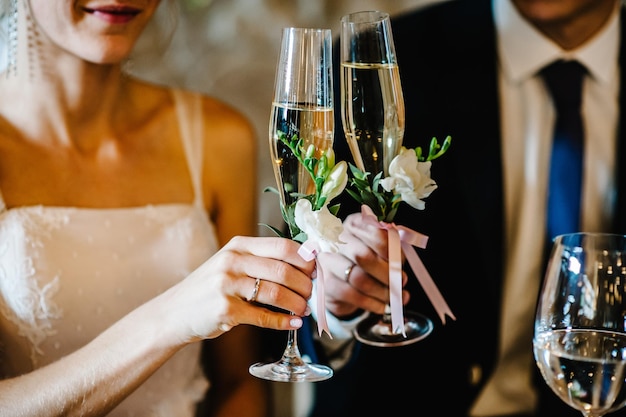 Glass decorated with flowers and greenery on the background newlyweds close up The bride and groom hold glasses of champagne in their hands Wedding ceremony