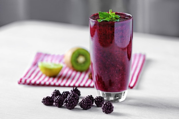 Glass of delicious blackberry milk shake on light table