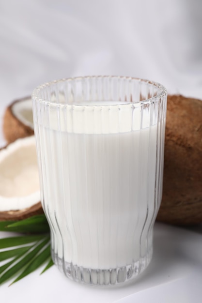 Glass of delicious coconut milk palm leaves and coconuts on white table