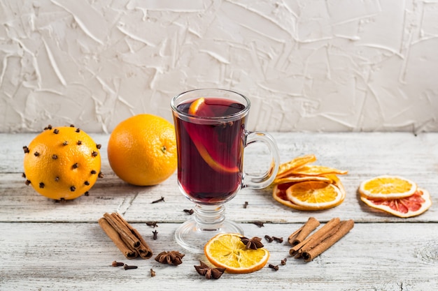 Glass of delicious mulled wine with oranges anise cinnamon on white wooden table