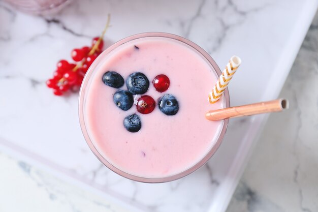 Glass of delicious smoothie with blueberry and cranberry on light wall, closeup