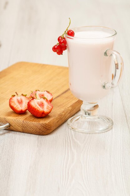 Glass of delicious strawberry yogurt with mint leaves and fresh strawberries on wooden cutting board