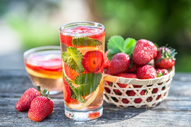 Glass of  detox water. Strawberry, lemon and mint with cool clean water, backdrop of a green garden.