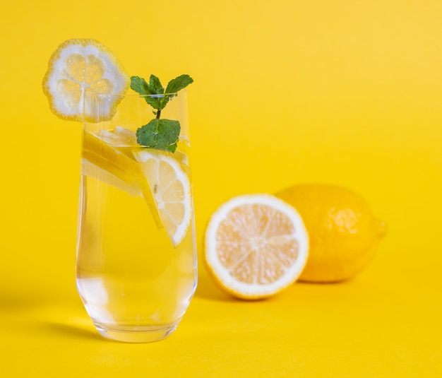 Glass of detox water with lemon slices and mint leave on yellow background