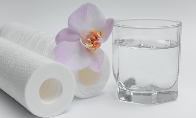 A glass of drink water and filter cartridges at white background