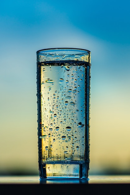 A glass of drinking water against the backdrop of the sunset sky.