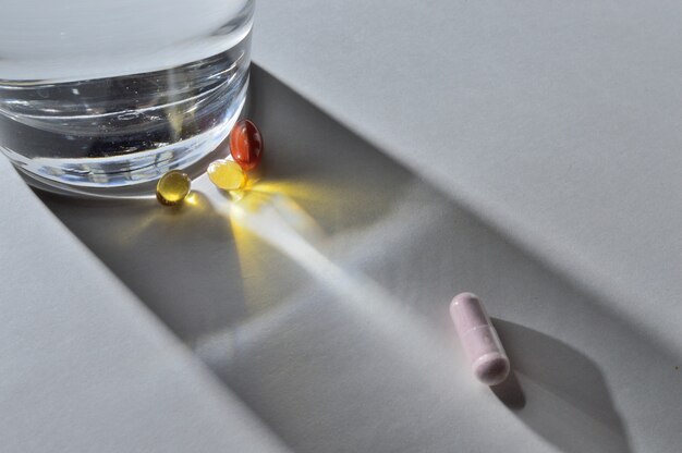 A glass of drinking water and several capsules with vitamins. light background. close-up.