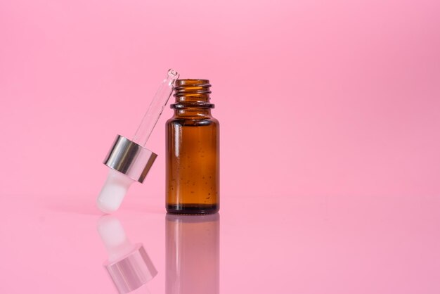 A glass dropper bottle on the pink background