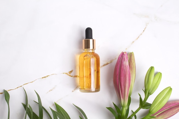 Glass dropper bottle with lily flowers on marble background Cosmetic container mockup Hyaluronic acid oil serum with collagen and peptides skin care product