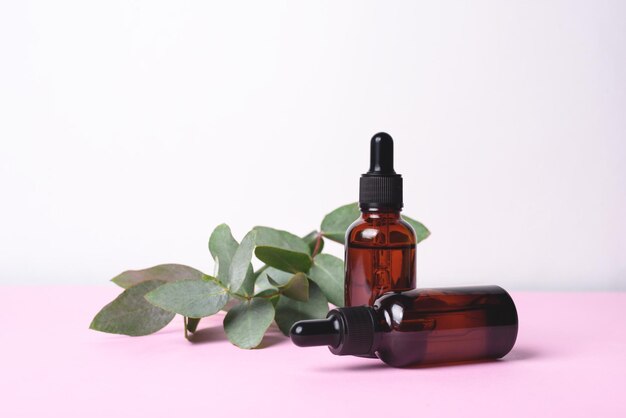 Glass dropper bottles and eucalyptus on pink and white background