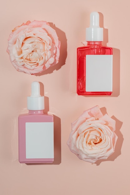 glass dropper bottles on trendy pastel peach background with flower heads of rose Abstract cosmetics composition with roses Beauty layout Summer aroma water concept