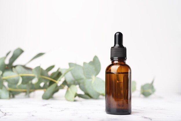 Glass dropper bottles on the white marble and eucalyptus background