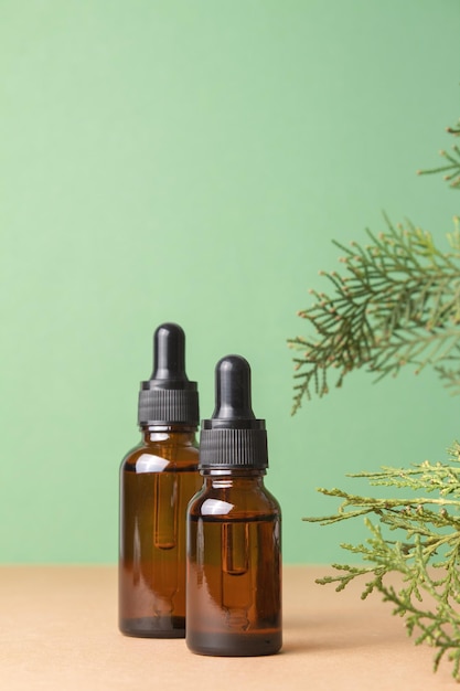 Glass dropper bottles with cosmetic oil essential or serum on green background with thuja branches Concept of natural organic cosmetics Herbal homeopathic products