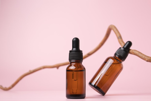 Glass dropper bottles with cosmetic oil essential or serum on pastel background with branch tree