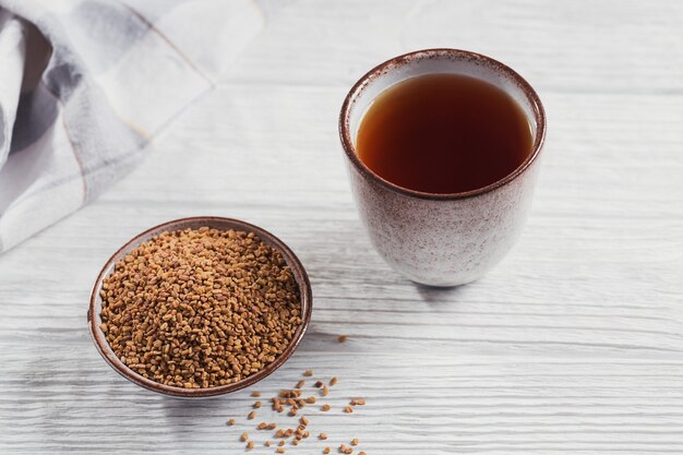 Glass of Egyptian fenugreek yellow tea, Helba or Methi Dana drink and fenugreek seeds on white wooden background