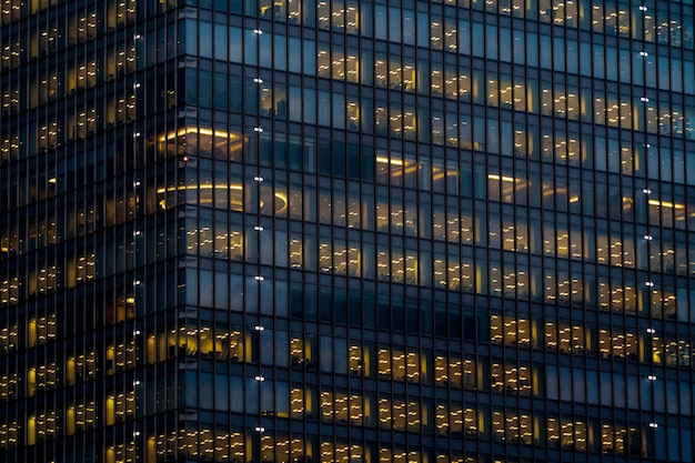 Glass exterior facade with interior yellow lighting glow in each floor in a skycraper