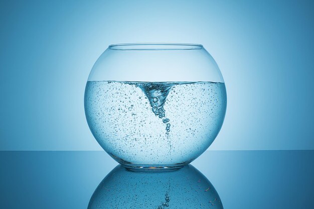 A glass fishbowl with a little swirl in the water on blue background. Taken in Studio with a 5D mark III.