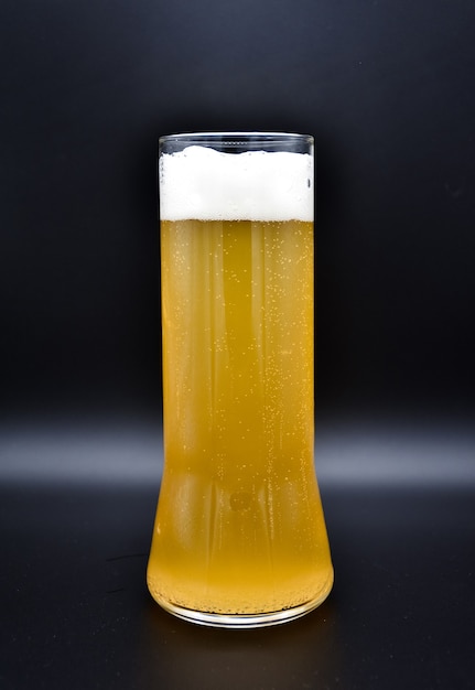 Glass flask on a black surface with yellow liquid and white foam, a glass of beer