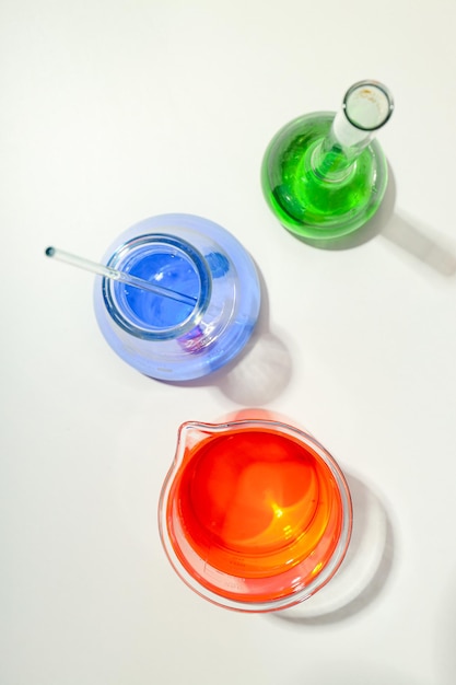 Glass flasks with colorful liquids on white background top view