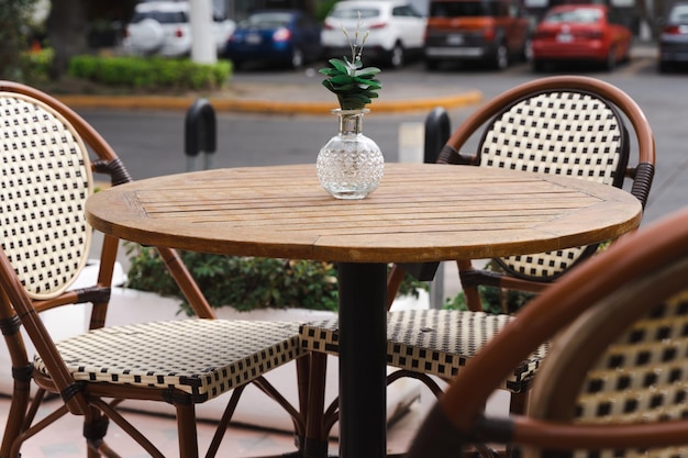 Glass flowerpot on wooden table and empty chairs at cafe terrace. Low season, outdoor decoration