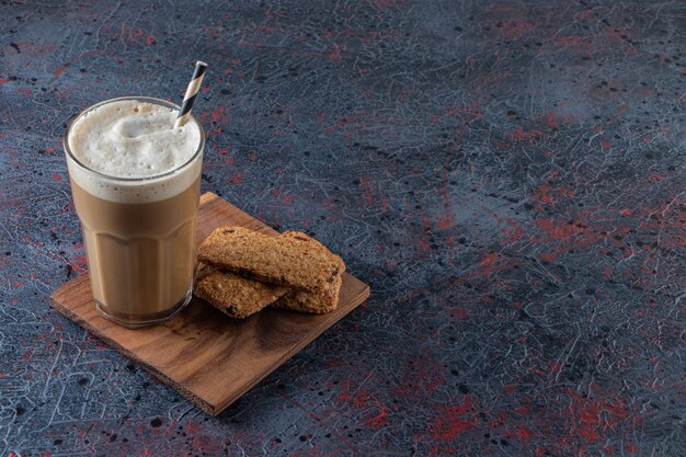 Glass of foamy cold coffee with biscuits on wooden plate. 