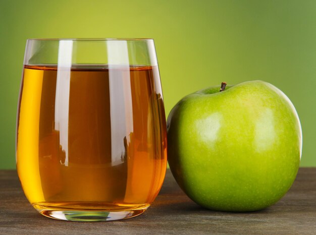 Photo glass of fresh apple juice on table on green background