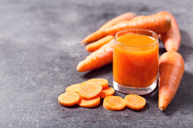 Glass of fresh carrot juice with vegetables on dark 