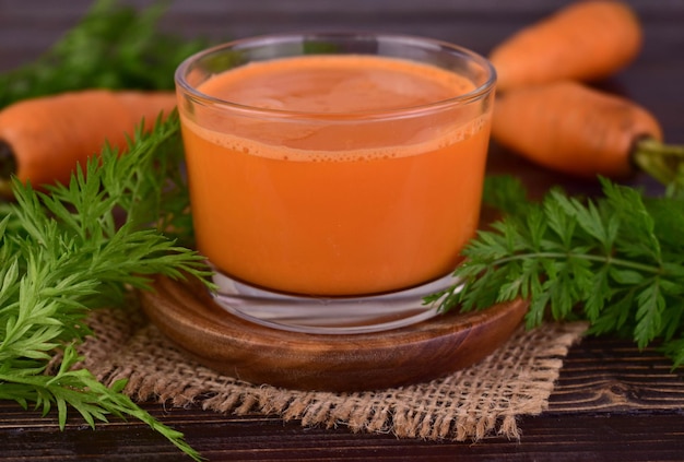 A glass of fresh carrot juice on a wooden trayCloseup