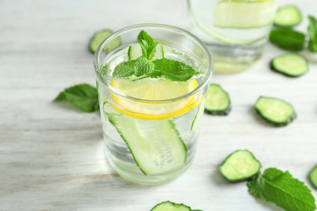 Glass of fresh cucumber water with lemon and mint on table