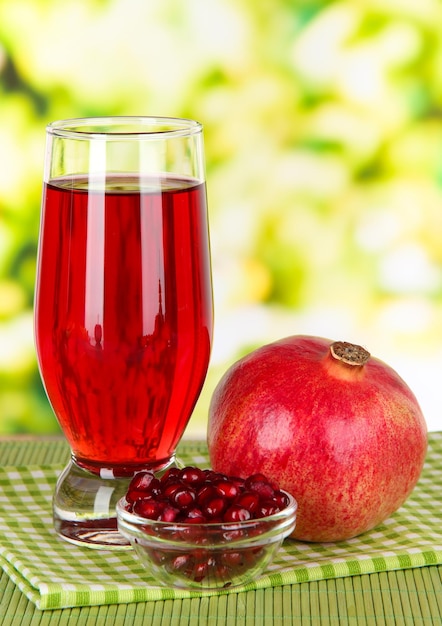 Glass of fresh garnet juice on table on bright background