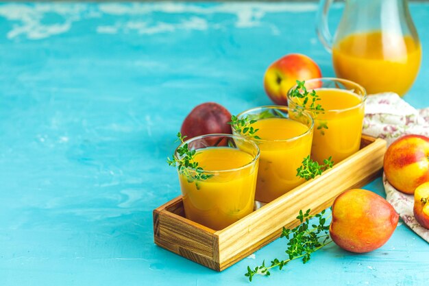 Glass of fresh healthy peach smoothie or juice in wooden box on light blue concrete surface table shallow depth of the field close up copy space for you text