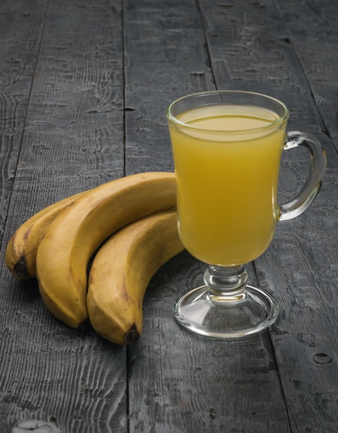 A glass of fresh juice and bananas on a wooden table