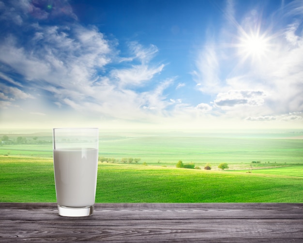 Photo glass of fresh milk against wavy green pasture