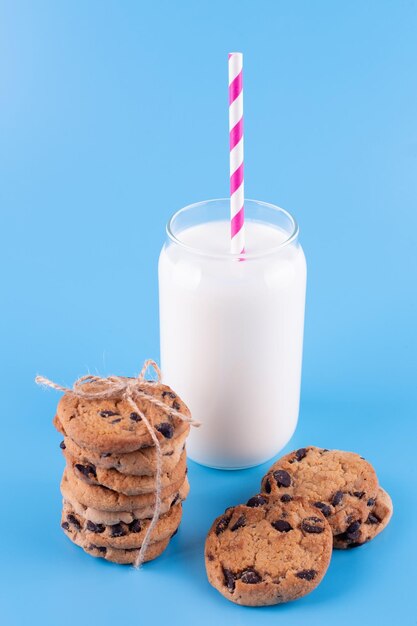 Glass of fresh milk with straw and brown school chocolate cookies blue background sweet food yummy