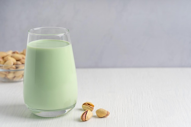 Glass of fresh non dairy vegan pistachio milk served with seeds on white wooden background