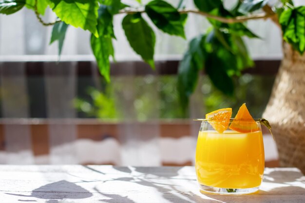 Glass of fresh orange juice garnished with a slice of orange on the white wooden table in the summer terrace