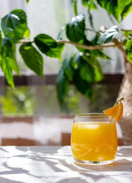 여름 테라스의 흰색 나무 테이블에 오렌지 조각으로 장식된 신선한 오렌지 주스 한 잔