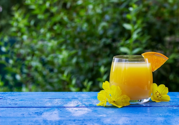 Glass of fresh orange juice garnished with a slice of ripe orange and flowers on the blue wooden table