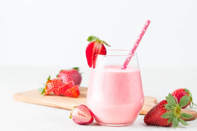 Glass of fresh strawberry milkshake, smoothie and fresh strawberries on pink, white and wooden background. Healthy food and drink concept.