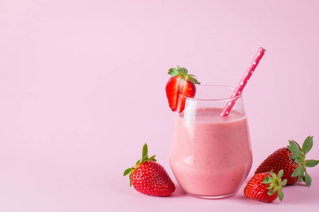 Glass of fresh strawberry milkshake, smoothie and fresh strawberries on pink, white and wooden background. Healthy food and drink concept.