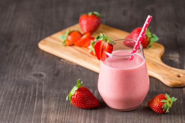 Glass of fresh strawberry milkshake, smoothie and fresh strawberries on pink, white and wooden background. Healthy food and drink concept.