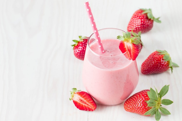 Glass of fresh strawberry milkshake, smoothie and fresh strawberries on pink, white and wooden background. Healthy food and drink concept.