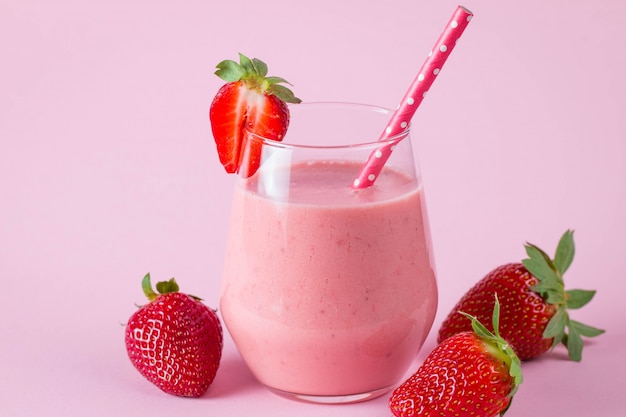 Glass of fresh strawberry milkshake, smoothie and fresh strawberries on pink, white and wooden background. Healthy food and drink concept.